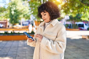 Parkta akıllı telefon kullanarak gülümseyen güzel bir İspanyol kadın.