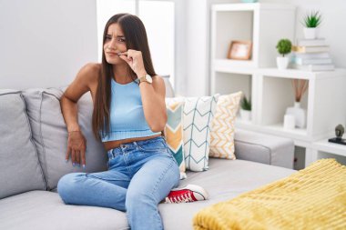 Genç esmer kadın kanepede oturuyor ev ağzında ve dudakları parmaklarıyla fermuar gibi kapalı. gizli ve sessiz, tabu konuşması 