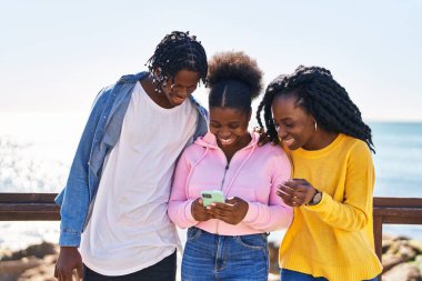 African american friends standing together using smartphone at seaside