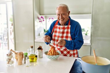 Son sınıf öğrencisi gülümsüyor. Mutfakta domates sosuyla spagettiyi karıştırıyor.