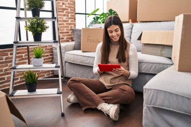 Genç ve güzel İspanyol kadın dokunmatik ped kullanıyor. Yeni evinde yerde oturuyor.