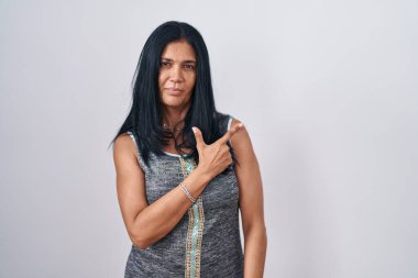 Olgun İspanyol bir kadın beyaz arka planda neşeli duruyor. Yüzünde mutlu ve doğal bir ifadeyle elleri ve parmaklarıyla gülümsüyor. 