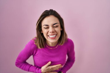 Pembe arka planda duran İspanyol kadın gülümsüyor ve kahkahalarla gülüyor çünkü elleri vücutta komik bir şaka var.. 