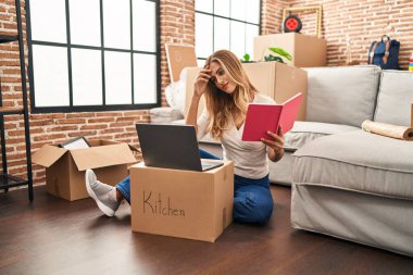 Genç sarışın kadın yeni evinde dizüstü bilgisayar okuyor.