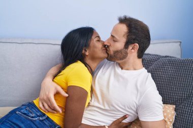 Man and woman interracial couple lying on sofa kissing at home