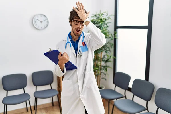 Young hispanic doctor man at waiting room surprised with hand on head for mistake, remember error. forgot, bad memory concept.
