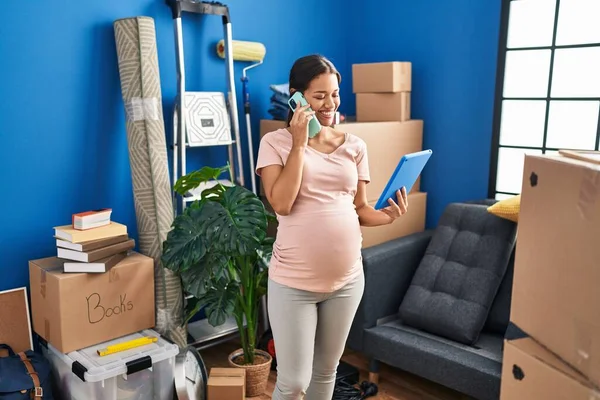若いですラテン女性妊娠使用してタッチパッドを話す上のスマートフォンで新しい家 — ストック写真