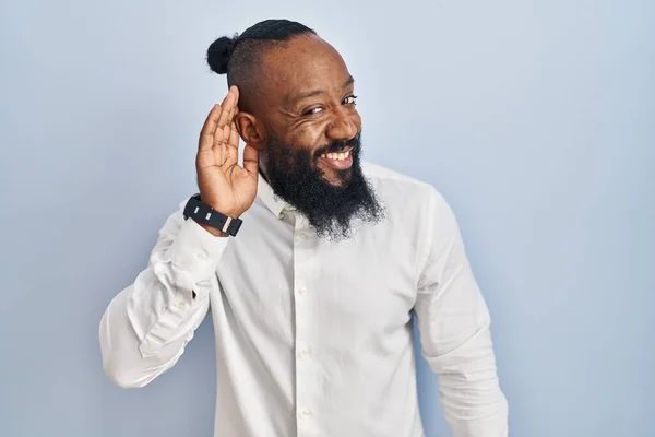 アフリカ系アメリカ人の男性は 噂やゴシップに耳を傾け 手で笑みを浮かべて青い背景に立っている 聴覚障害の概念 — ストック写真