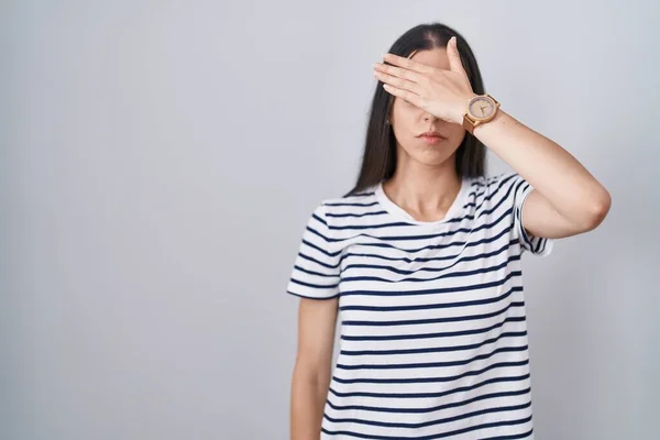 年轻的黑发女人穿着条纹T恤 用手捂住眼睛 看起来严肃而忧郁 躲藏和拒绝的概念 — 图库照片