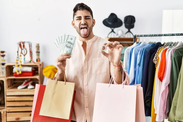 Young Hispanic Man Holding Shopping Bags Dollars Bitcoin Sticking Tongue — Zdjęcie stockowe