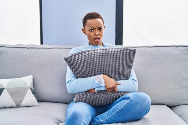 非洲裔美国妇女坐在沙发上 抱着枕头 毫无头绪 困惑的表情 怀疑概念 — 图库照片