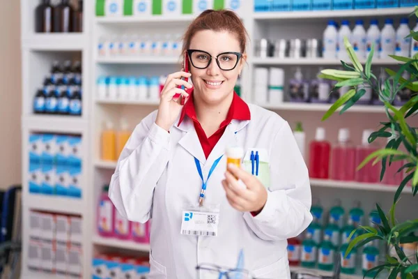 Young Beautiful Size Woman Pharmacist Holding Pills Bottle Talking Smartphone — Zdjęcie stockowe