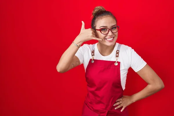 Jonge Spaanse Vrouw Draagt Serveerster Schort Rode Achtergrond Glimlachend Telefoongebaar — Stockfoto