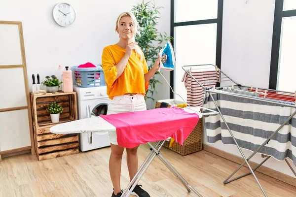 Young Caucasian Woman Ironing Clothes Home Serious Face Thinking Question — Stock Photo, Image