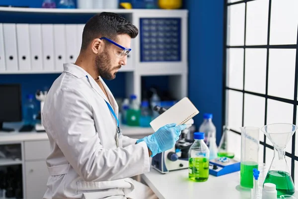 Young Hispanic Man Wearing Scientist Uniform Reading Book Laboratory — Stock Photo, Image
