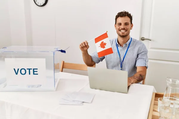 Joven Hispano Sonriendo Confiado Sosteniendo Bandera Canadá Trabajando Colegio Electoral —  Fotos de Stock