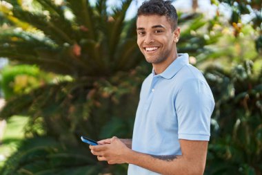 Afro-Amerikalı adam parkta akıllı telefon kullanarak kendine güveniyor.