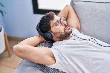 Genç İspanyol adam evdeki kanepede rahat bir şekilde müzik dinliyor.