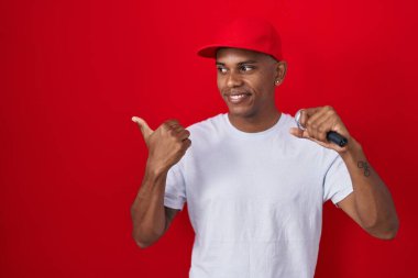 Genç İspanyol adam mikrofonla şarkı söylüyor başparmağıyla yan tarafa uzanıyor ve ağzı açık gülümsüyor. 