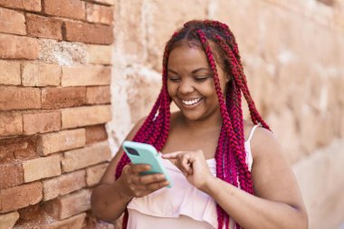 Afro-Amerikalı kadın sokakta akıllı telefon kullanarak kendine güveniyor.