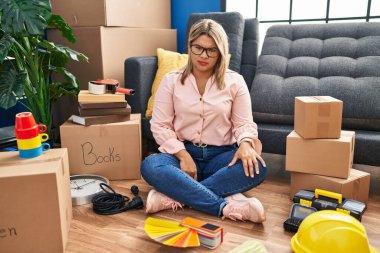 Young hispanic woman moving to a new home sitting on the floor skeptic and nervous, frowning upset because of problem. negative person. 
