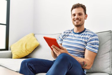 Young hispanic man smiling confident using touchpad at home