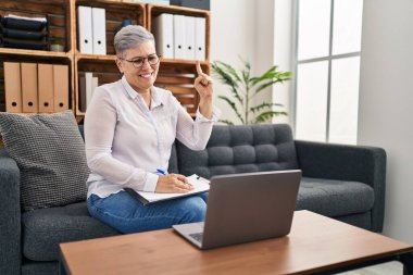 Orta yaşlı bir kadın danışmanlık ofisinde gülümsüyor. Bir fikir veya soru işareti ile gülümsüyor. Bir numara: 