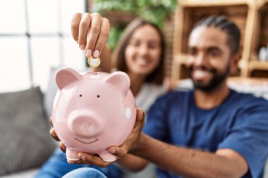 Man and woman couple smiling confident insert coin on piggy bank at home