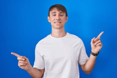 Caucasian blond man standing over blue background smiling confident pointing with fingers to different directions. copy space for advertisement 