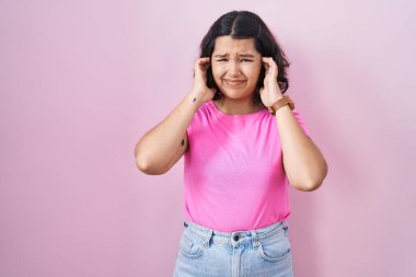 Pembe arka planda duran genç İspanyol kadın yüksek sesli müzik sesi için parmaklarıyla kulaklarını kapatıyor. sağır kavramı. 