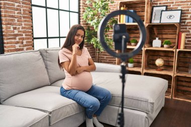 Genç hamile bir kadın akıllı telefonuyla video kaydı yapıyor. Ciddi bir yüz ifadesi var. Çene ve çeneyle soru sormayı düşünüyor. 