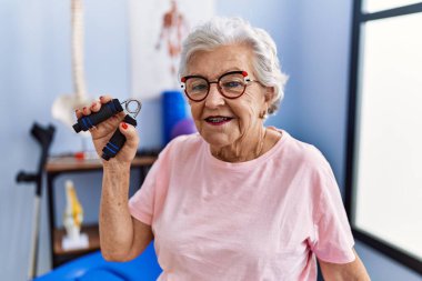 Yaşlı gri saçlı kadın fizyoterapist terapi kliniğinde el ele tutuşarak rehabilitasyon seansı yapıyor.