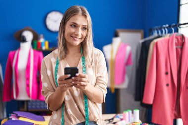 Young caucasian woman tailor smiling confident using smartphone at sewing studio