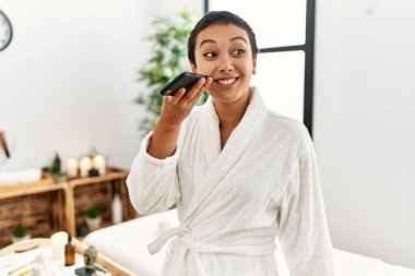 Bornoz giyen genç İspanyol kadın güzellik merkezindeki akıllı telefondan sesli mesaj gönderiyor.