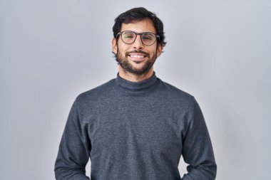 Handsome latin man standing over isolated background with hands together and crossed fingers smiling relaxed and cheerful. success and optimistic 