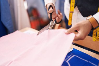 Young hispanic man tailor cutting cloth at atelier