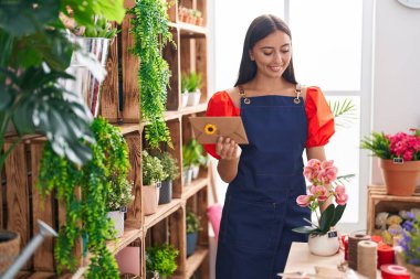 Young beautiful hispanic woman florist holding envelope letter and plant at florist
