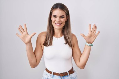 Hispanic young woman standing over white background showing and pointing up with fingers number ten while smiling confident and happy. 