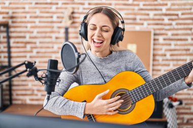 Genç kadın sanatçı müzik stüdyosunda klasik gitar çalarak şarkı söylüyor.