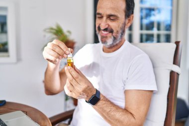 Orta yaşlı bir adam terasta dizüstü bilgisayar kullanıp şurup içiyor.