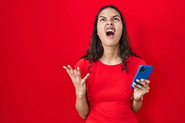 Młoda Brazylijka Pomocą Smartfona Czerwonym Tle Szalony Szalony Krzyki Krzyki — Zdjęcie stockowe