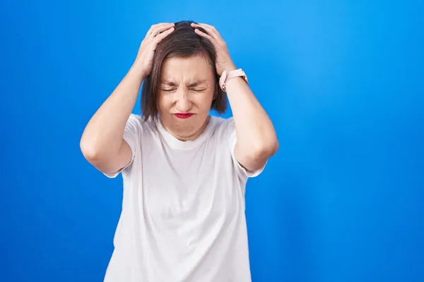 中年惊慌失措的女人站在蓝色的背景上 由于疼痛和偏头痛 绝望和压力重重 手放在头上 — 图库照片