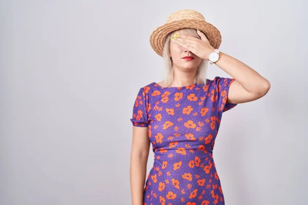 年轻的高加索女人穿着花衣服 戴着夏帽 用手捂住眼睛 看起来严肃而忧郁 躲藏和拒绝的概念 — 图库照片