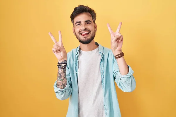 Young Hispanic Man Tattoos Standing Yellow Background Smiling Tongue Out — Stok fotoğraf