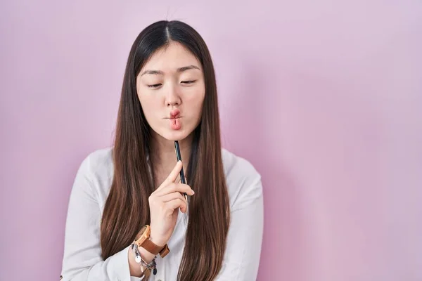 中国年轻女子用铅笔捂住粉红的背景 用嘴和眼神做鱼脸 疯狂而滑稽 — 图库照片
