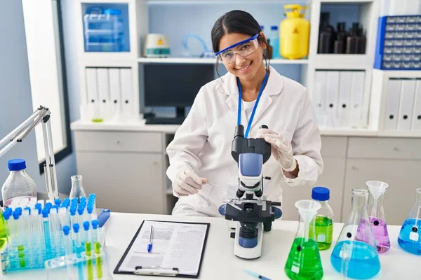 研究室で顕微鏡を使って科学者の制服を着た若いラテン語の女性 — ストック写真