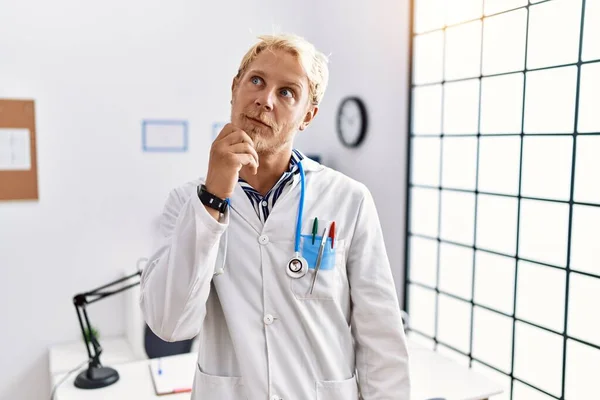 Młody Blondyn Mundurze Doktora Stetoskopie Klinice Ręką Podbródku Myślący Pytaniu — Zdjęcie stockowe