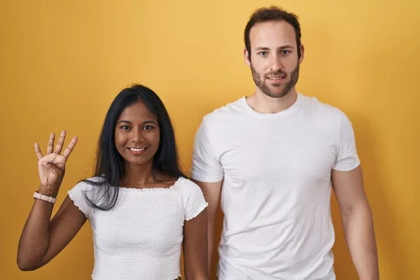 Interracial Couple Standing Yellow Background Showing Pointing Fingers Number Four — 图库照片