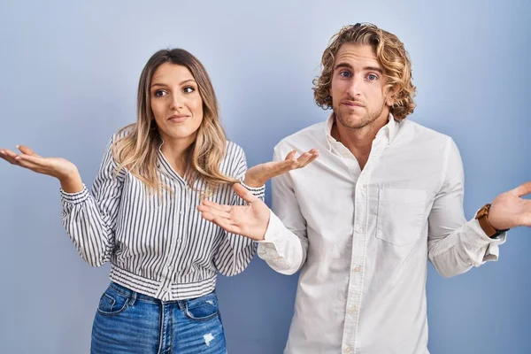Young Couple Standing Blue Background Clueless Confused Expression Arms Hands — Stockfoto