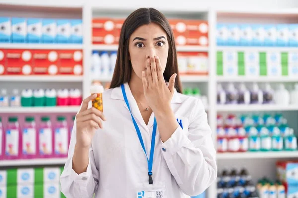 薬局で働くヒスパニック系の女性は 手で口をカバー薬を保持し ショックを受け 間違いを恐れています 驚きの表情 — ストック写真